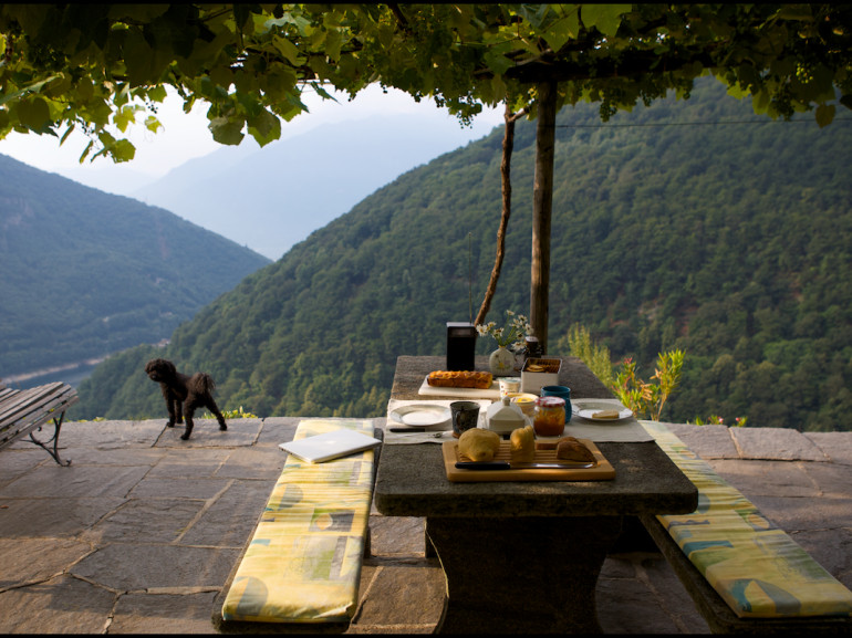 tavolo di legno preparato per la colazione su un terrazzo vista lago tra verdi colline