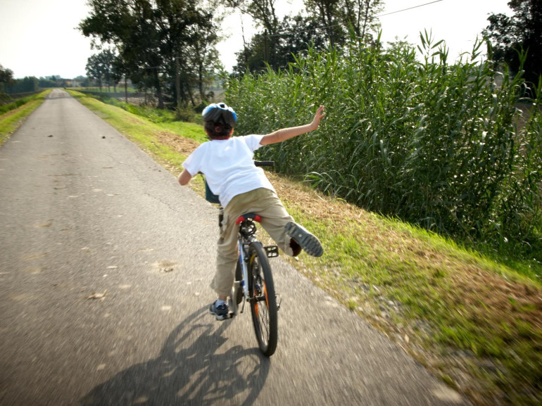 un bambino corre in bicicletta su una pista ciclabile che costeggia un prato