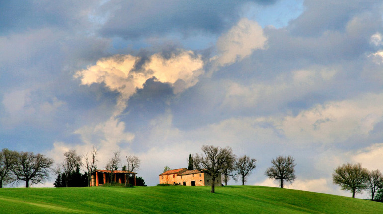 colline ricoperte di erba verde, un casale e il cielo con le nuvole dopo il temporale