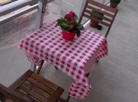 Tavolo con tovaglia a scacchi rossi e bianchi con mazzo fiori rossi e sedie su un patio di Maha via Flickr