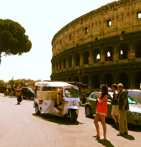 Persone ammirano un tuk tuk bianco feermo davanti al Colosseo