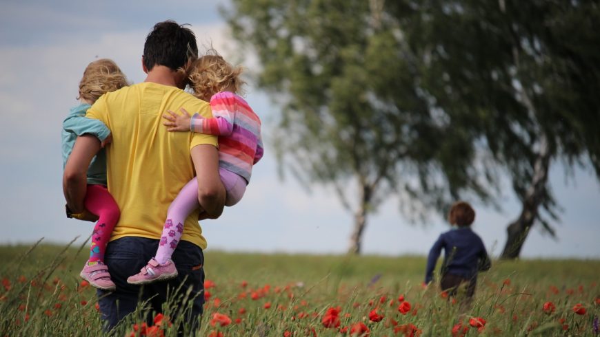 un uomo con due bambini in braccio in un campo di fiori