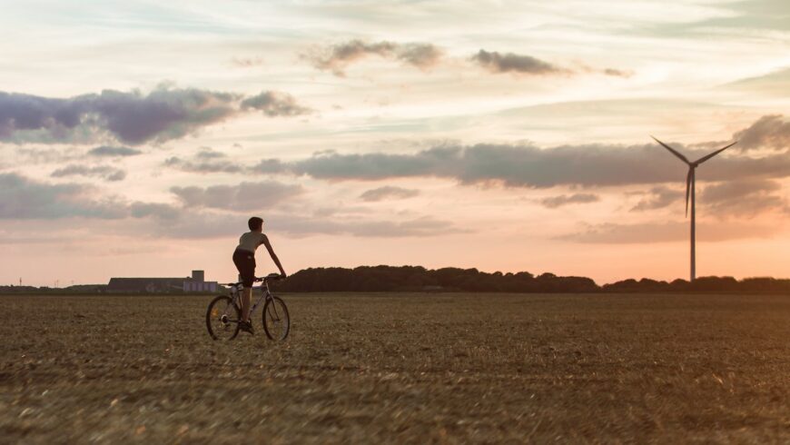 Una persona su una bicicletta in un campo da una turbina eolica