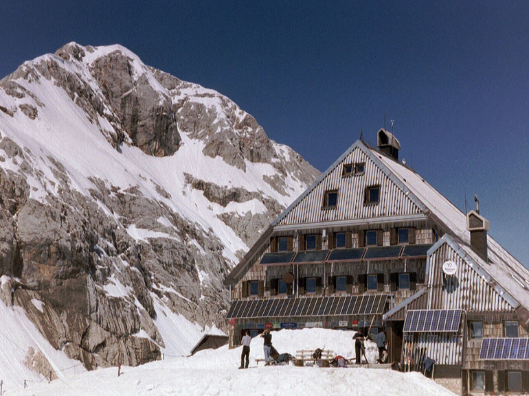 rifugio alpino tra la neve, ai piedi di una cima rocciosa