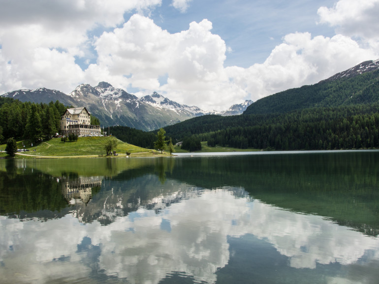 spettacolari montagne innevate si specchiano su un limpido lago, circondato da verdi colline
