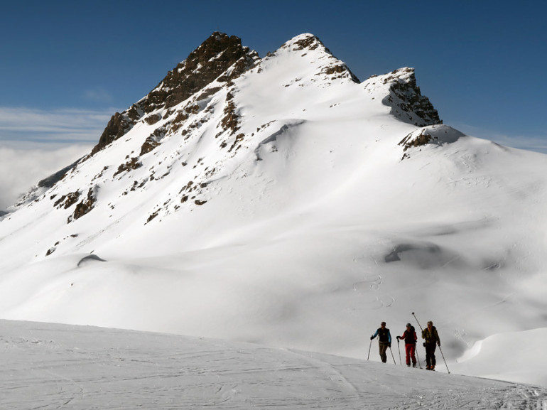 tre camminatori nel bianco della neve sotto una cima rocciosa